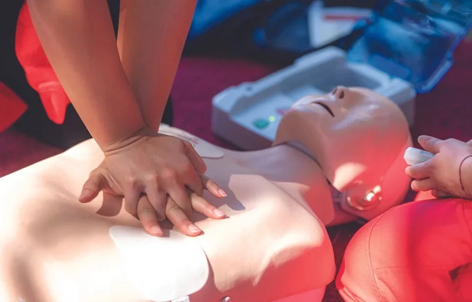 Participants practicing chest compressions on a CPR manikin with AED training equipment nearby