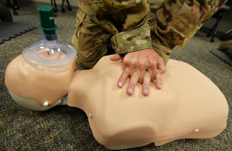 A person in military uniform practicing chest compressions on a CPR manikin